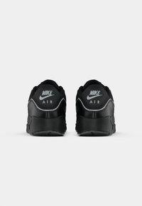 Sneaker Nike Air neri con una texture liscia, caratterizzati da una forma tondeggiante, collare imbottito e logo prominente sul tallone.
