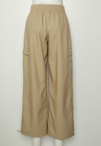 Pantalon cargo beige à jambes larges avec taille élastique, poches à rabat latérales et ourlets ajustables, présenté sur un mannequin blanc devant un fond uni.