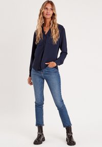 Marineblå langærmet skjorte med et tekstureret mønster, knaplukning fortil, to brystlommer, parret med lyseblå jeans og sorte ankelstøvler.