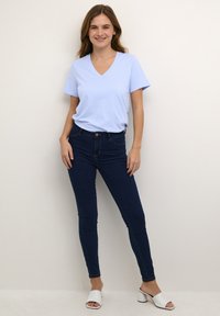 Světle modré tričko s výstřihem do V v kombinaci s tmavě modrými skinny džíny a bílými sandály na podpatku. Hladký materiál a přiléhavý střih.