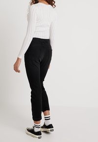 Svarta högmidjade jeans med bakfickor, åtsittande design, uppvikta benslut, tillsammans med svarta sneakers och vitrandiga strumpor.