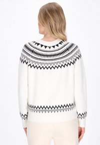 Maglione bianco con motivi geometrici neri a maglia attorno al giromanica e ai polsini. Tessuto morbido, orlo a costine e vestibilità leggermente oversize.