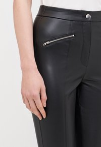 Svarta läderbyxor med en stilren design, hög midja och en ficka med dragkedja på höger sida, med slät matt yta.