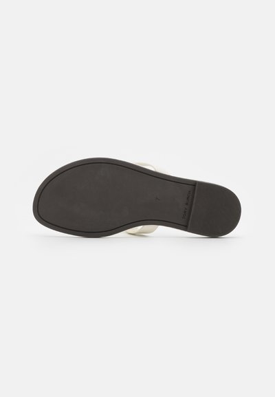 Semelle en caoutchouc noir avec une surface texturée et un léger talon. La partie supérieure présente des brides ivoire lisses. Taille 7 indiquée sur la semelle intérieure.