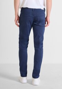 Jean azul marino con un ajuste slim, diseño de cinco bolsillos y una textura suave. Acabado con costuras sutiles y sin logos visibles.