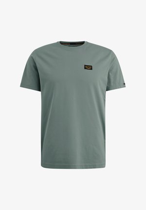 Vihreä puuvillapaita, jossa on pyöreä kaula-aukko, lyhyet hihat ja pieni musta logo-patch rinnassa. Sujuva rakenne, rento istuvuus.