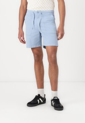 Shorts bleu clair en coton, avec une taille à cordon de serrage, deux poches latérales et une coupe décontractée, associés à des baskets noires.