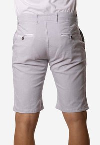 Vista trasera de una persona que lleva pantalones cortos de rodilla de color gris claro con bolsillos traseros abotonados y pasadores de cinturón.