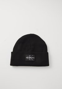 Zwarte gebreide beanie met omgeslagen rand. Bevat een rechthoekige zwarte patch met de witte tekst "Calvin Klein Jeans" en het grijze "CK"-logo. Zachte textuur.