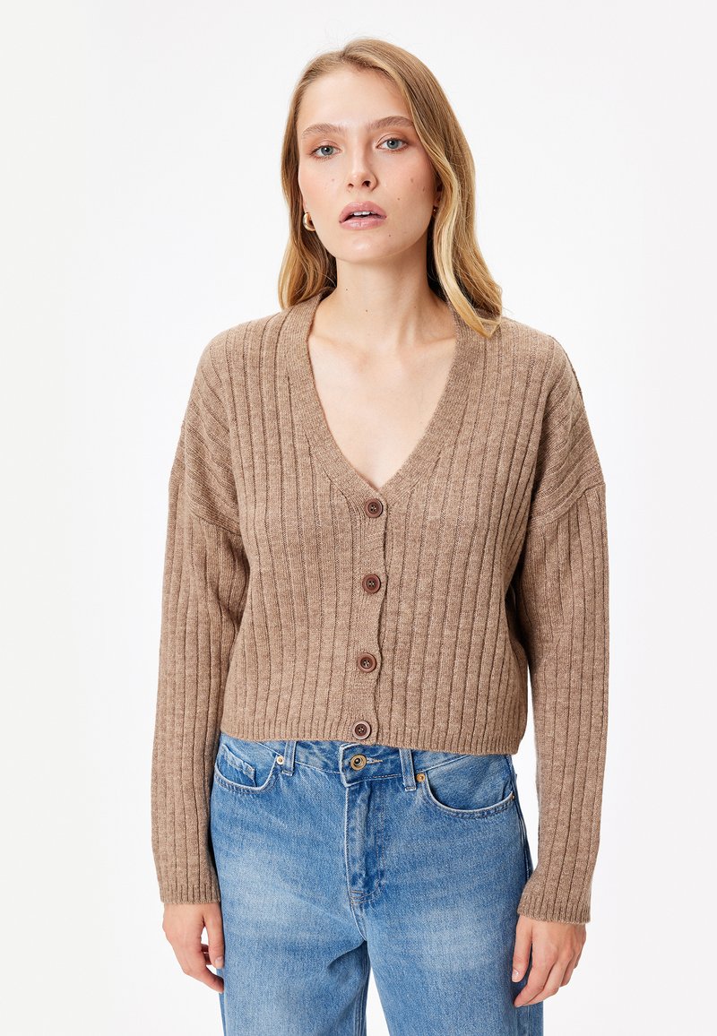 Bruine geribbelde cardigan met een diepe V-hals, knopen aan de voorkant en lange mouwen. Draag het met lichtblauwe high-waisted jeans. Gladde textuur.