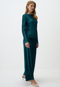 Completo due pezzi turchese composto da una maglietta a maniche lunghe con righe verticali e pantaloni a gamba larga, realizzati in tessuto morbido. Tacchi a punta color nude.