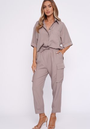 Frau trägt taupefarbenes locker sitzendes Kurzarmhemd mit Knöpfen und passende hoch taillierte Cargohosen mit beigen Sandalen mit hohen Absätzen.