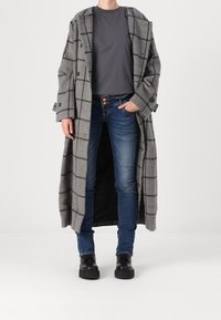 Abrigo de cuadro gris hecho de mezcla de lana, de longitud hasta la rodilla con grandes solapas, combinado con una camiseta gris y jeans de mezclilla azules, completado con zapatos negros.
