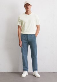 Hellgelbes Baumwoll-T-Shirt, gerade geschnittene blaue Chinos und weiße Sneaker. Lässiges Outfit mit einfachen Linien und weichen Texturen.