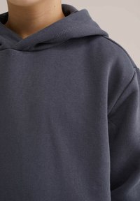 Ciemnoszara, bawełniana bluza z kapturem, wykonana z miękkiego materiału, charakteryzująca się prostym, bezszwowym wzorem i luźnym krojem.