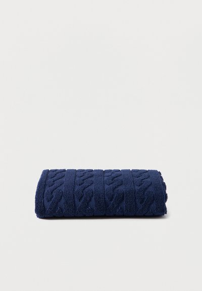 Σκουρό μπλε διπλωμένη πετσέτα με υφή και ριγέ σχέδιο σε απλό ανοιχτό φόντο.