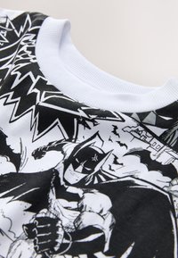 Svart och vit grafisk T-shirt med en Batman-design i seriestil, vit ribbad rund hals, och textil med struktur.
