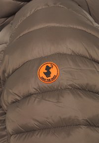 Braune gepolsterte Jacke mit einem runden orangen Patch, der ein schwarzes Entenmotiv und den Text "SAVE THE DUCK" zeigt, wobei die gesteppte Textur hervorgehoben wird.