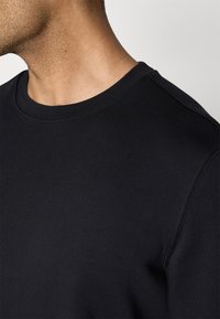 Sweat-shirt noir en coton avec col rond, manches courtes, détails de couture apparents et texture lisse, présenté de profil.