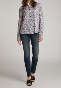 Camicia a fiori con bottoni nei toni del blu, rosa e verde; abbinata a jeans skinny in denim scuro; scarpe slip-on nere open-toe.