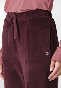 Bordeaux velours joggers met een elastische tailleband en trekkoord, voorzien van zijzakken en een klein logoaccent nabij de zoom.