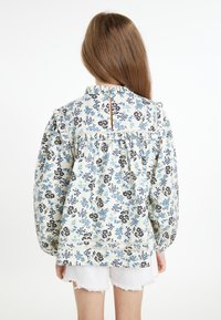 Blusa con stampa floreale e colletto a ruffle, sfondo azzurro chiaro, fiori blu scuro e neri, schiena a chiave, vita arricciata e maniche lunghe.