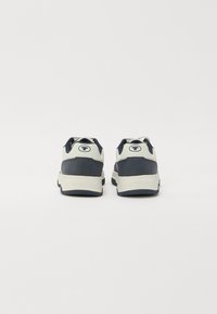 Zapatillas deportivas con suela acolchada, que presentan una combinación de colores azul marino y crema, material texturizado y detalles de logotipo en la parte posterior.