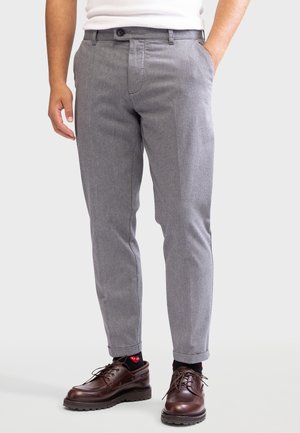 Slim-Fit graue Hose, getragen mit schwarzen Socken mit roten Herzlogos und dunkelbraunen Leder-Schnürschuhen.