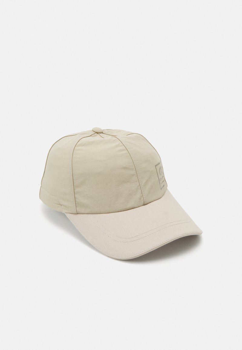 Boné de beisebol bege feito de material leve, com uma aba curva, coroa arredondada e um patch de logo costurado no painel da frente.