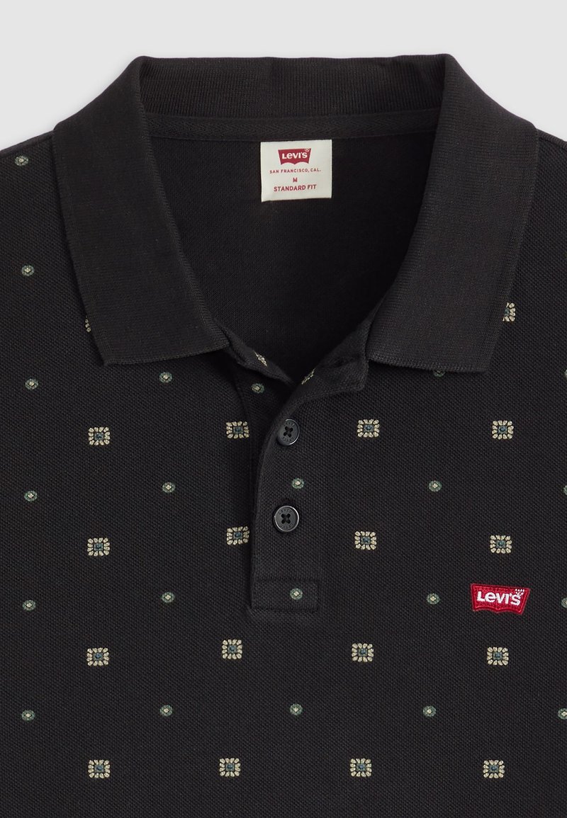 Schwarzes Poloshirt aus strukturiertem Stoff mit kleinen geometrischen Mustern in Creme und Grün. Dreiknopf-Leiste; rotes Logo-Label am Saum.