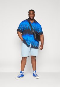 T-skjorte med kort erme med blå flamme mønster over en svart bakgrunn, kombinert med lyse denimshorts og blå høye sneakers. Svart crossover-veske.