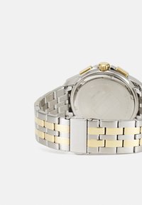 Montre en acier inoxydable avec un bracelet en argent et en or. Boîtier rond et dos transparent, avec une couronne en or et des accents de fermoir.