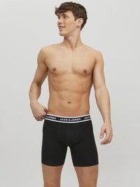 Schwarze Boxer-Briefs mit einem weißen Markenbund, auf dem "JACK & JONES" steht. Der Stoff wirkt glatt und körperbetont. Keine Muster.