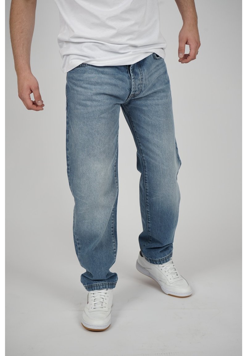 Vaaleansiniset farkut rennolla istuvuudella, suoran lahkeen, haalistuneen pinnan ja korostettujen lahkeiden kanssa. Yhdistetty valkoisiin tennareihin.