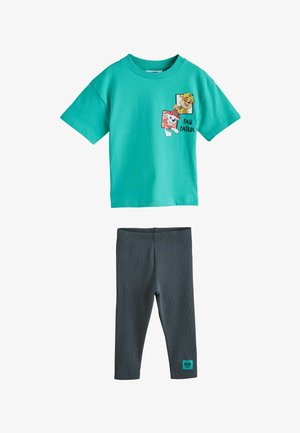 Tirkizna majica kratkih rukava s likovima pasa iz crtića Paw Patrol i crne hlače s logotipom Paw Patrol na lijevoj nozi.