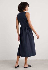 Navyblauwe mouwloze jurk met een aansluitend lijfje en een geplooide rok, gemaakt van lichtgewicht stof, die tot halverwege de kuit reikt.
