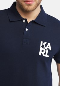 Marineblaue Poloshirt aus strukturiertem Material, mit klassischem Kragen, zwei Knöpfen und einem kontrastierenden weißen Logodesign auf der Brust.