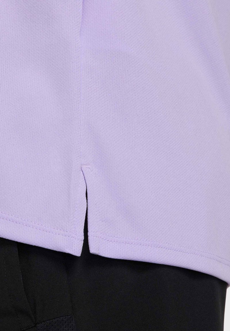 Gros plan sur l'ourlet en tissu lavande avec une petite fente latérale sur un pantalon noir, montrant les détails de la texture et des coutures.