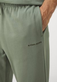 Zelene športne hlače iz mehkega materiala z elastičnim pasom in stranskimi žepi. Imajo diskreten logotip "BJÖRN BORG" v temno zeleni barvi.