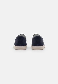 Sötétkék velúr slip-on cipők sima felülettel, egyszerű dizájnnal és bézs talppal. Nincsenek további minták vagy díszítések.