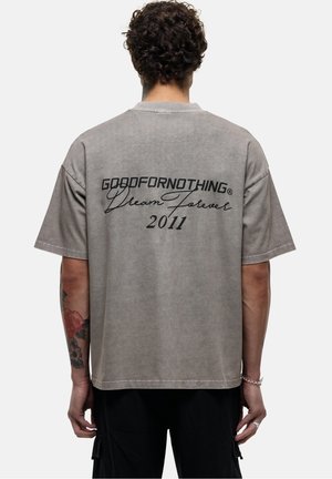 T-shirt oversize gris à manches courtes, avec les inscriptions "GOODFORNOTHING" et "Dream Forever 2011" en noir au dos. Tissu en coton.