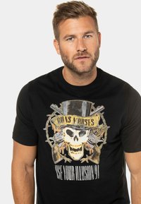 Černé bavlněné tričko s centrálním motivem lebky v cylindru, obklopené pistolemi a růžemi, s textem "GUNS N' ROSES" a "USE YOUR ILLUSION 91".