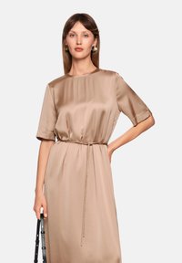 Satin, beige dress with short sleeves, round neckline, and drawstring waist. Holds a shoulder bag, featuring minimalistic design and smooth texture.