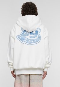 Felpa bianca con una grande grafica azzurro chiaro del numero "29", un razzo e stelle sul retro. Caratterizzata da una vestibilità ampia e rilassata.