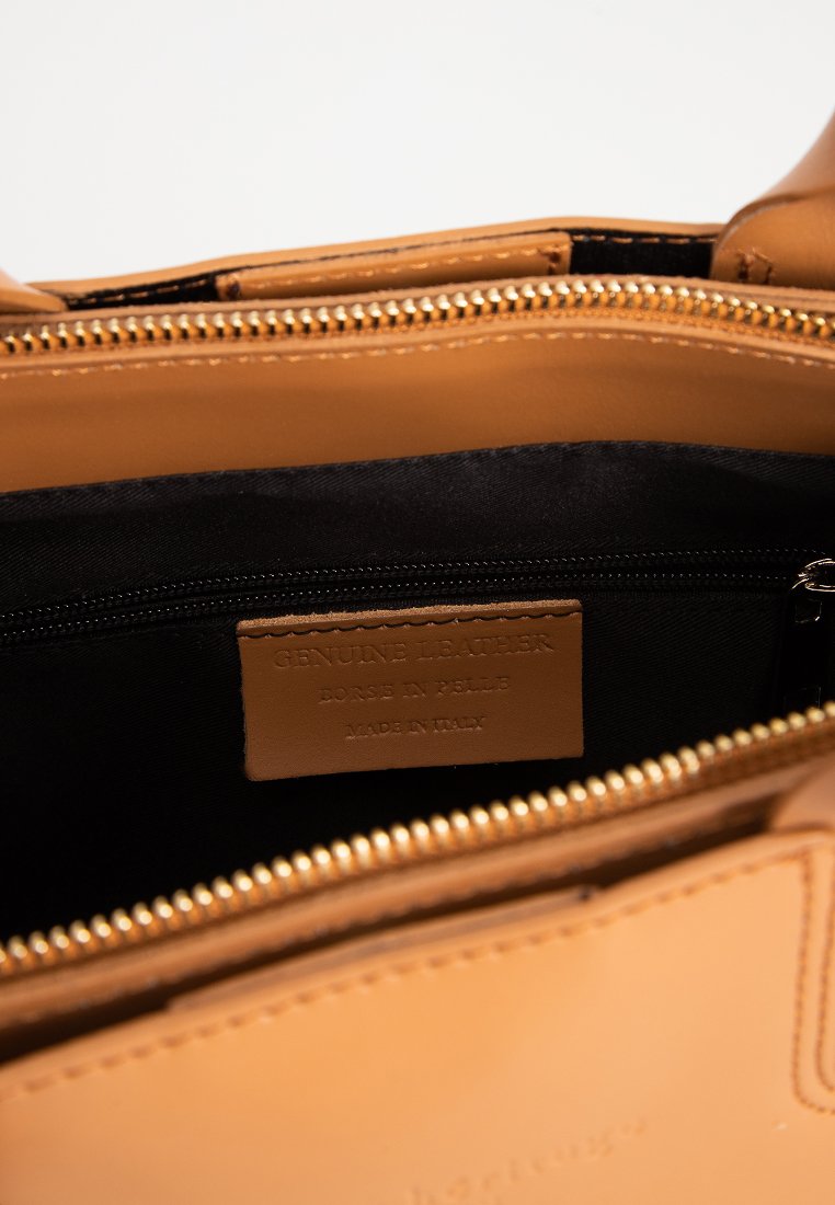 Handtasche aus echtem, tanfarbenem Leder mit einem Innenfutter aus schwarzem Stoff, goldenem Reißverschluss und einem Etikett, das Authentizität und Herkunft beschreibt.