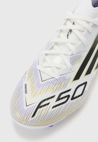 Crampons de soccer blancs avec des rayures dégradées violettes et dorées, tige texturée, logo "F50" noir et lacets. Présente une forme épurée et un design léger.