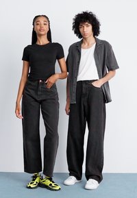 Svart kortermet t-skjorte, høytlivte svarte jeans med rød knapp, og oversized grå skjorte. Sko: gule-svarte joggesko, hvite joggesko.