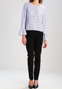 Blusa blu a righe con maniche a volant e dettagli ricamati, abbinata a pantaloni neri aderenti e tacchi neri.