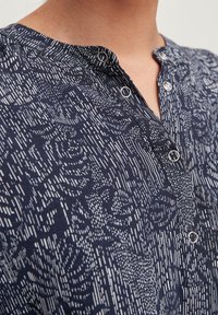 Camisa de botones azul marino con un patrón gráfico texturizado en blanco. Cuenta con un cuello redondeado y acentos de botones plateados.