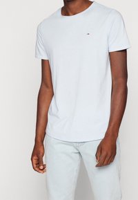 Světle modré bavlněné tričko s kulatým výstřihem, krátkými rukávy a malým logem na hrudi. Texturovaná tkanina, volný střih.